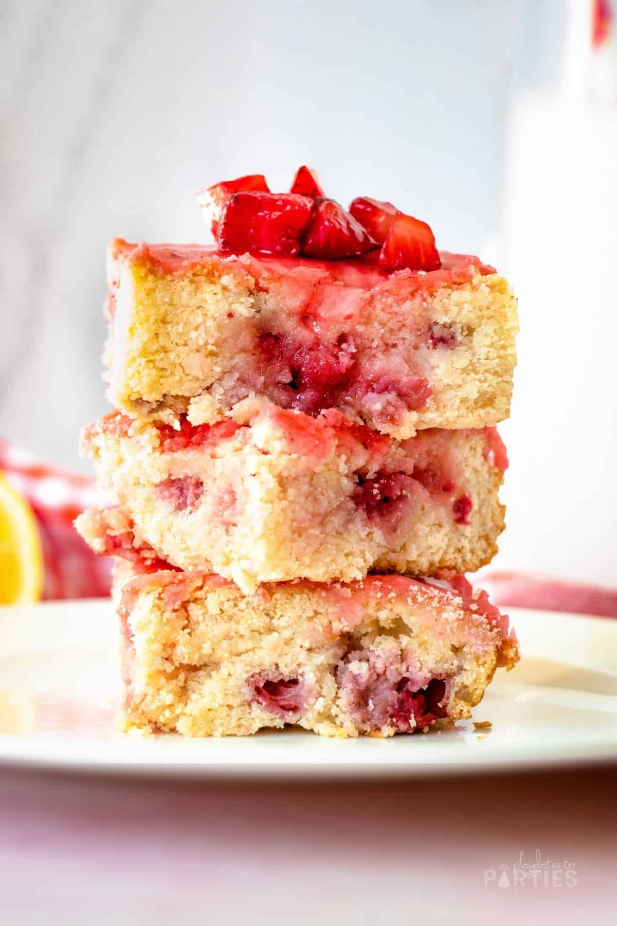 A stack of strawberry lemon bars on a plate, topped with fresh strawberries.
