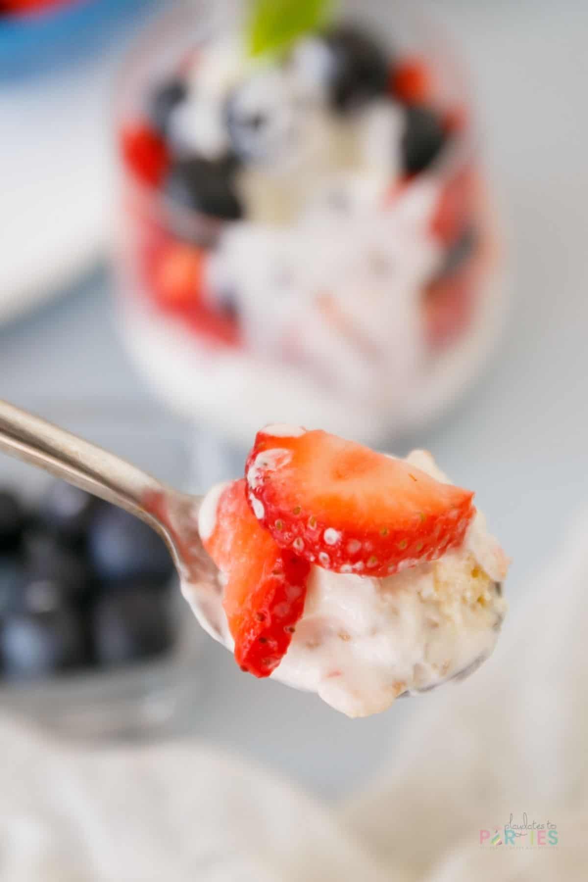Bite shot of a spoon with yogurt, granola, and strawberries.