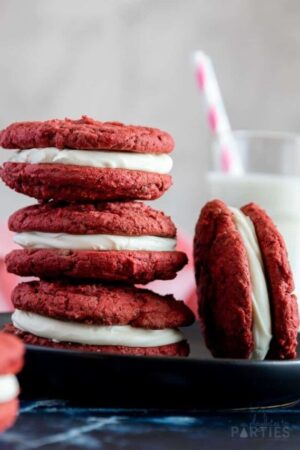 3 red velvet cookie sandwiches stacked on a small black plate.