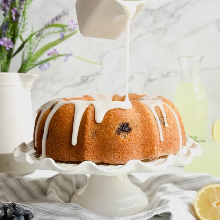 A woman's hand pouring glaze over a lemon bundt cake on a party platter.