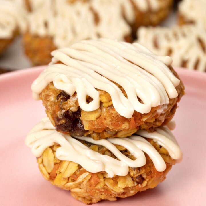 Thick carrot cake cookies with drizzled icing on a pink plate.