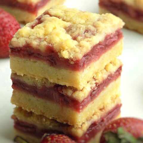 Strawberry crumble bars stacked up with fresh strawberries nearby.