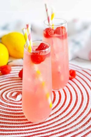 Two pink vodka lemonade cocktails surrounded by fresh lemons and raspberries.