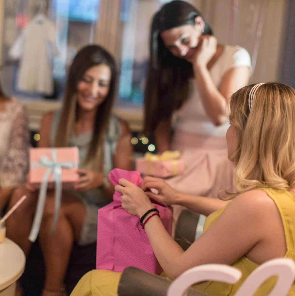 A pregnant woman in a yellow dress opens up gifts during a baby shower.