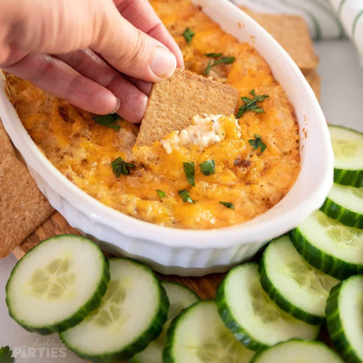 A woman's hand dipping a cracker into a bowl of Old Bay crab dip.