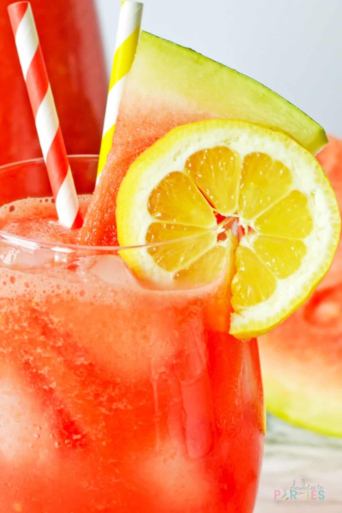 Close up image of a cup of watermelon lemonade with a slice of lemon and a wedge of watermelon.