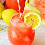 Homemade watermelon lemonade in a wine glass on a marble surface.