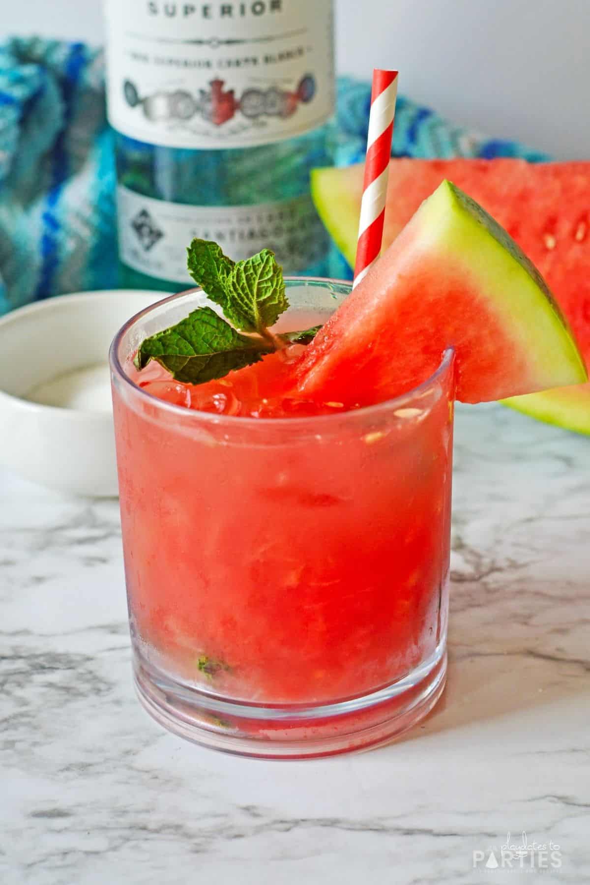 A red summer cocktail garnished with mint and fresh watermelon.
