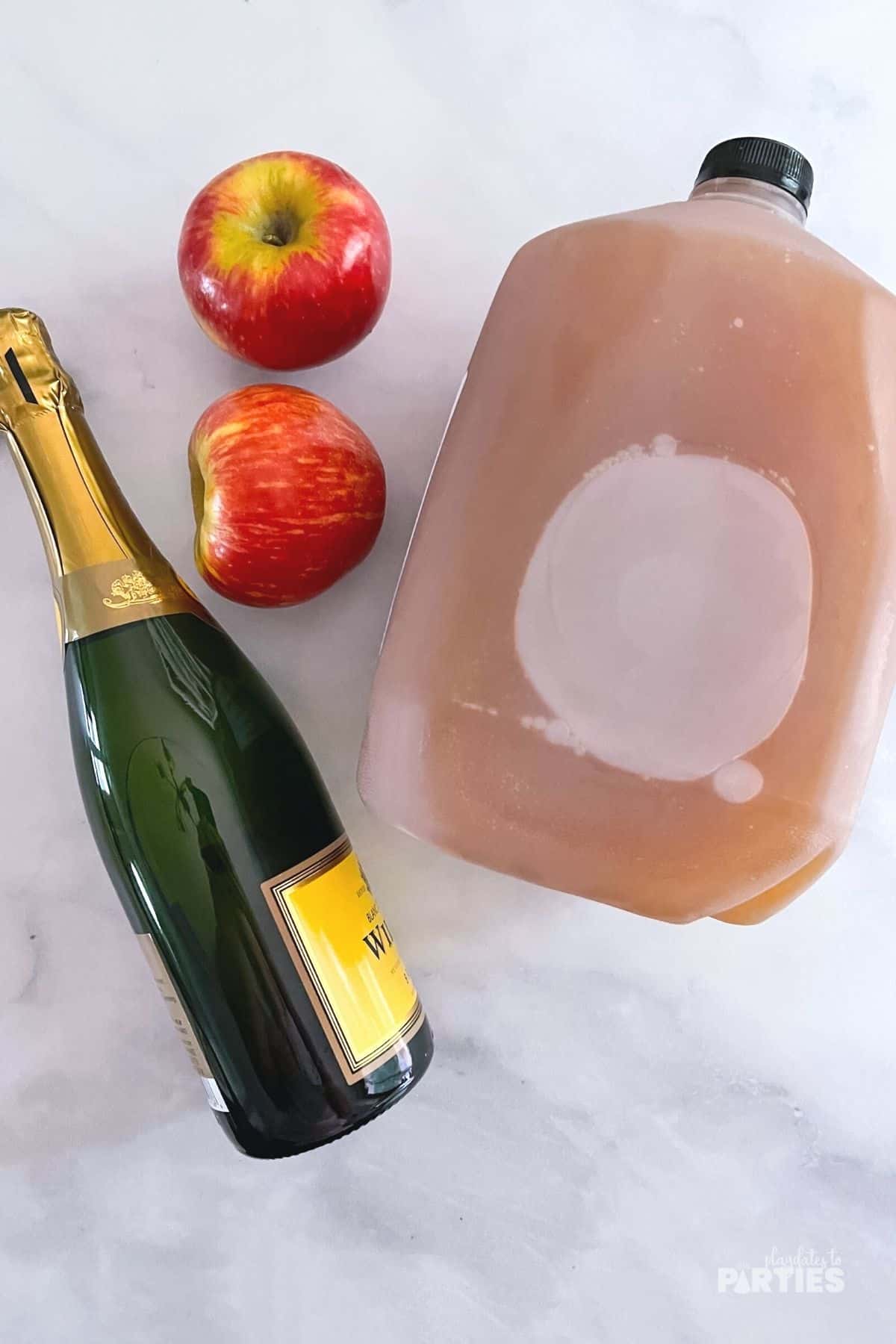 Ingredients on a marble surface include champagne, apples, and apple cider.