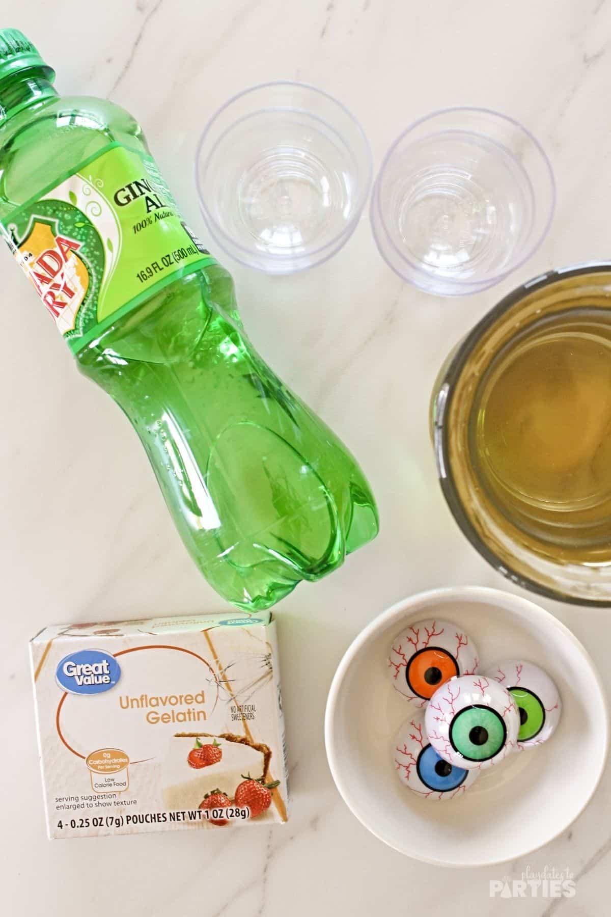 Ingredients on a table including ginger ale, unflavored gelatin, gummy eyeballs, and white grape juice.