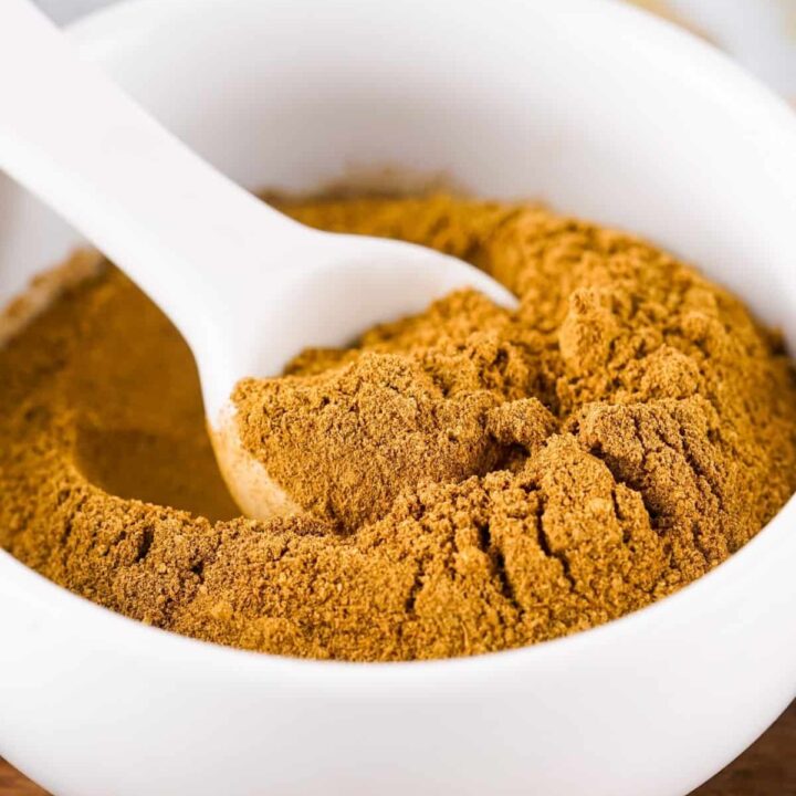 A measuring spoon scooping spice mix out of a white bowl.