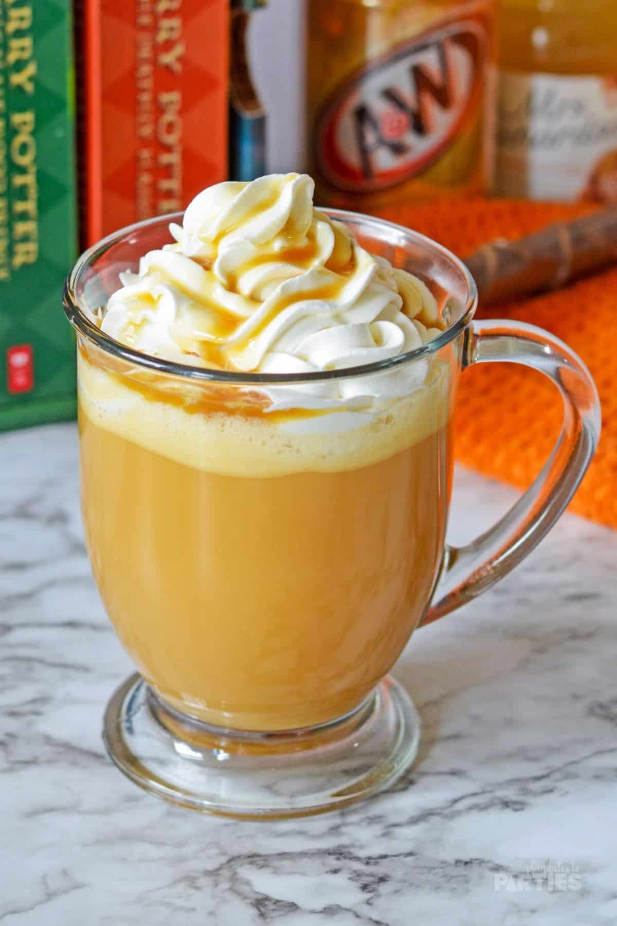 A mug of butterbeer sitting in front of Harry Potter books and a play wand.