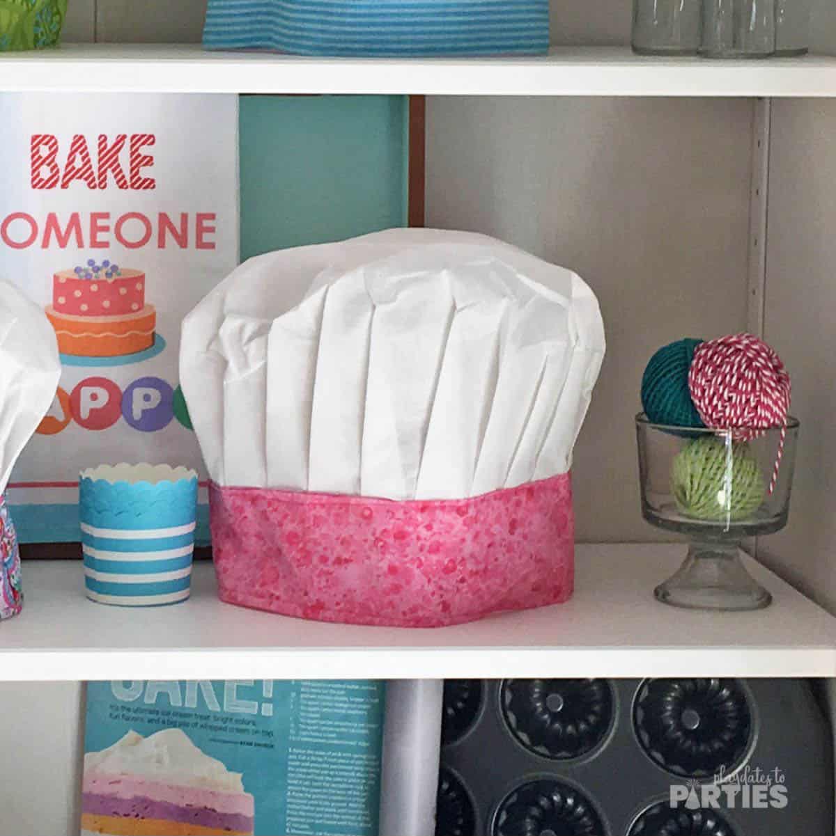 A fabric chef hat with a colorful band surrounded by baking supplies.