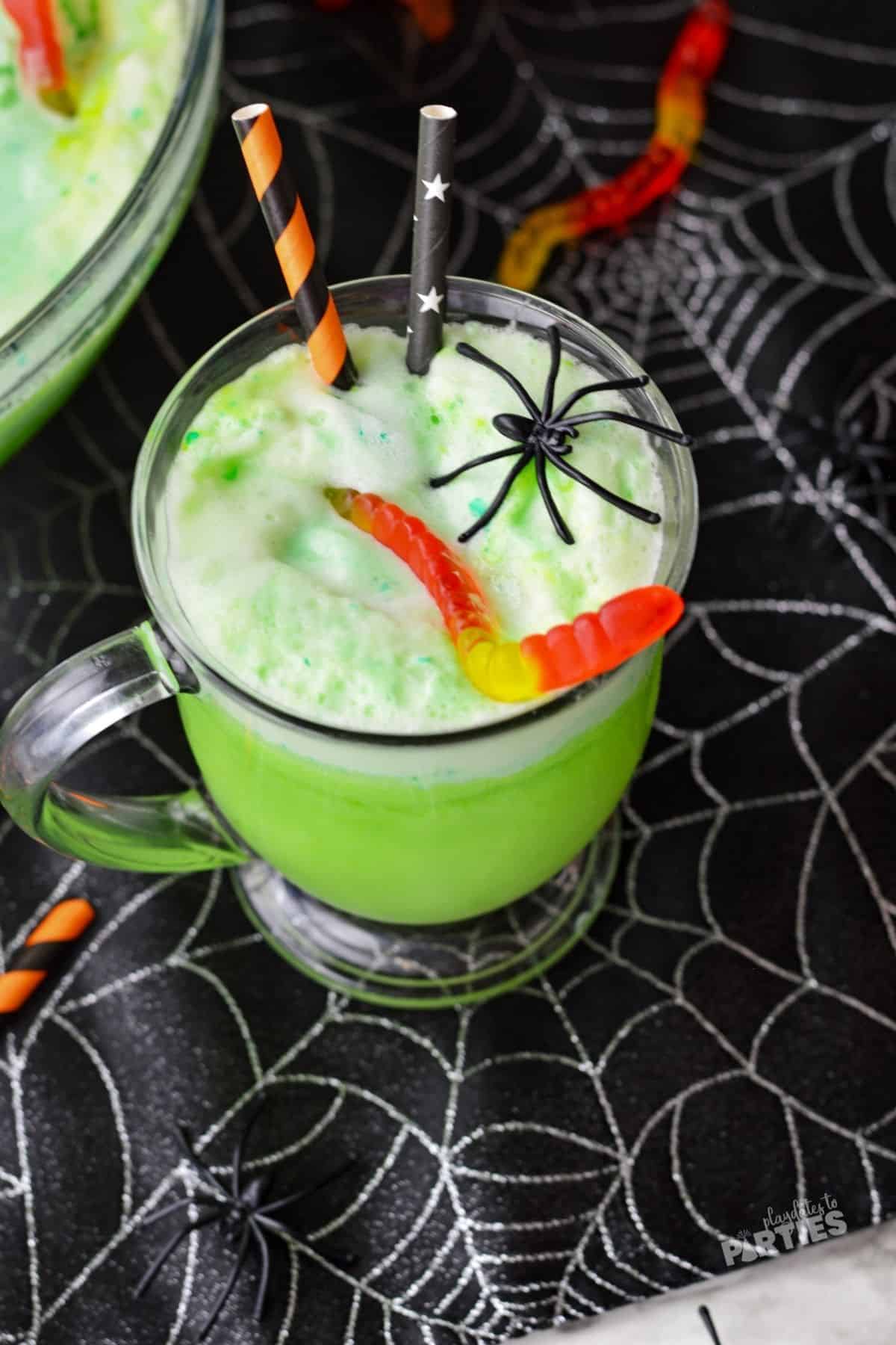 Top view of a glass mug filled with frothy green Halloween punch garnished with gummy worms and plastic spiders.