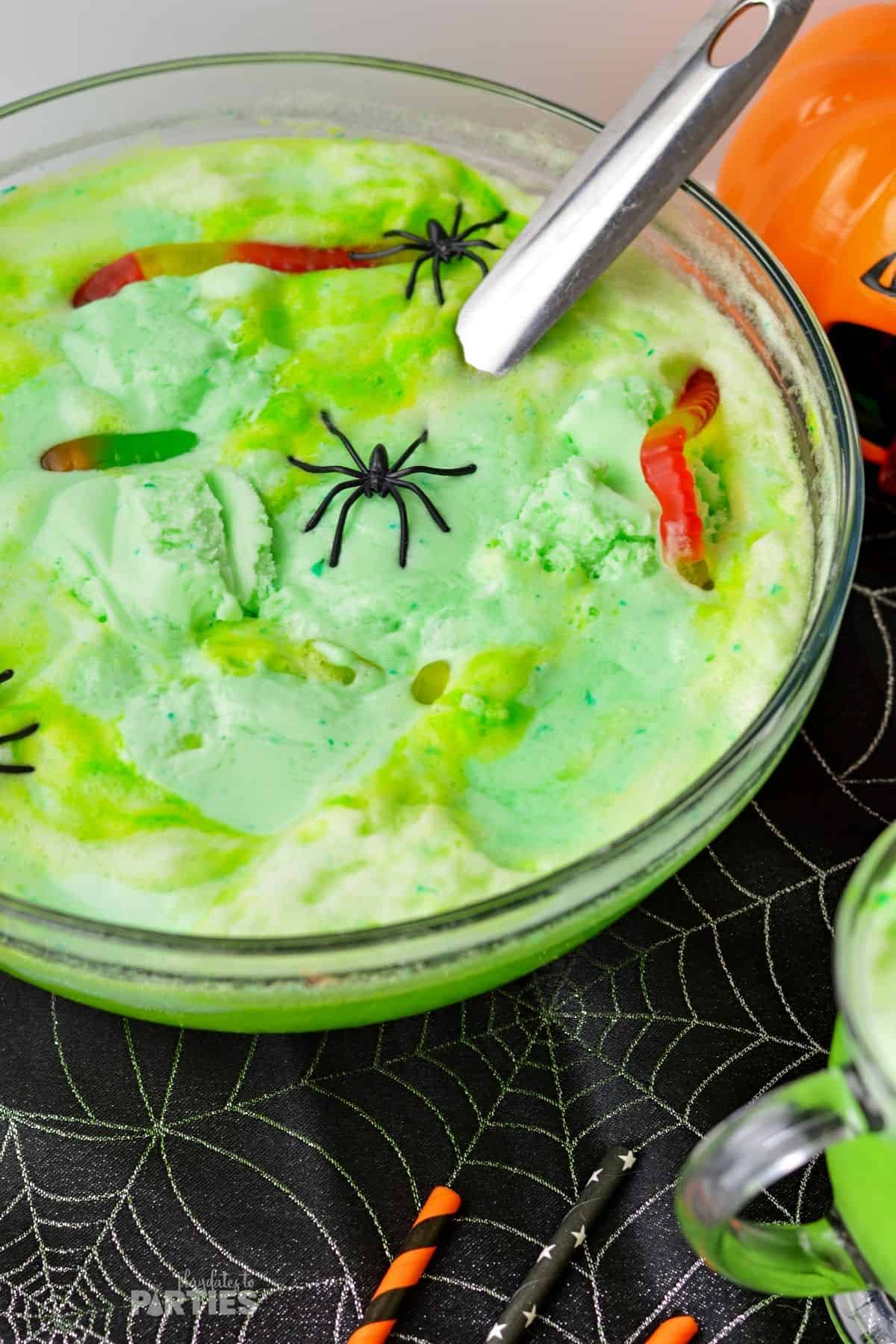 A bowl filled with frothy witches brew punch sits on a black Halloween party tablecloth.