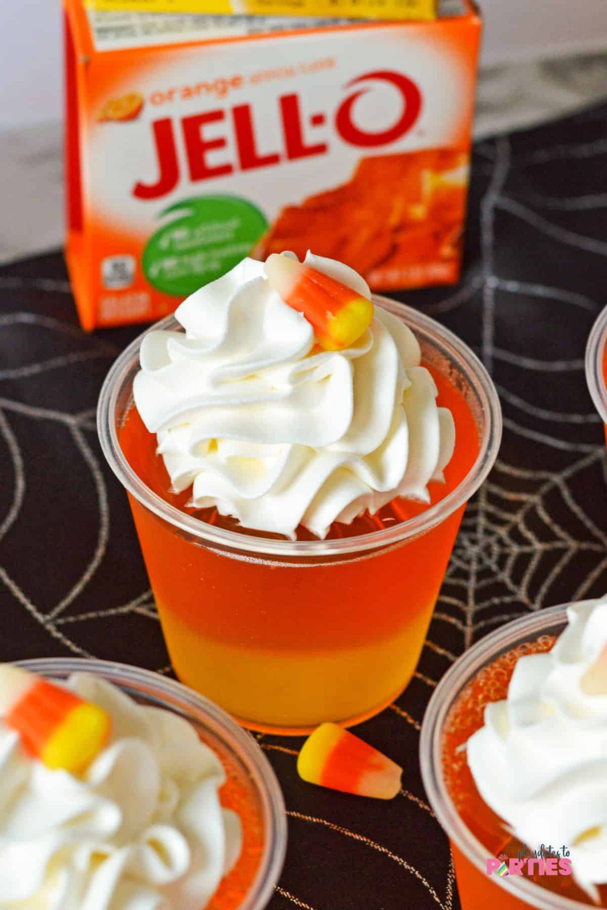A plastic cup with layers of yellow and orange jello topped with whipped cream.