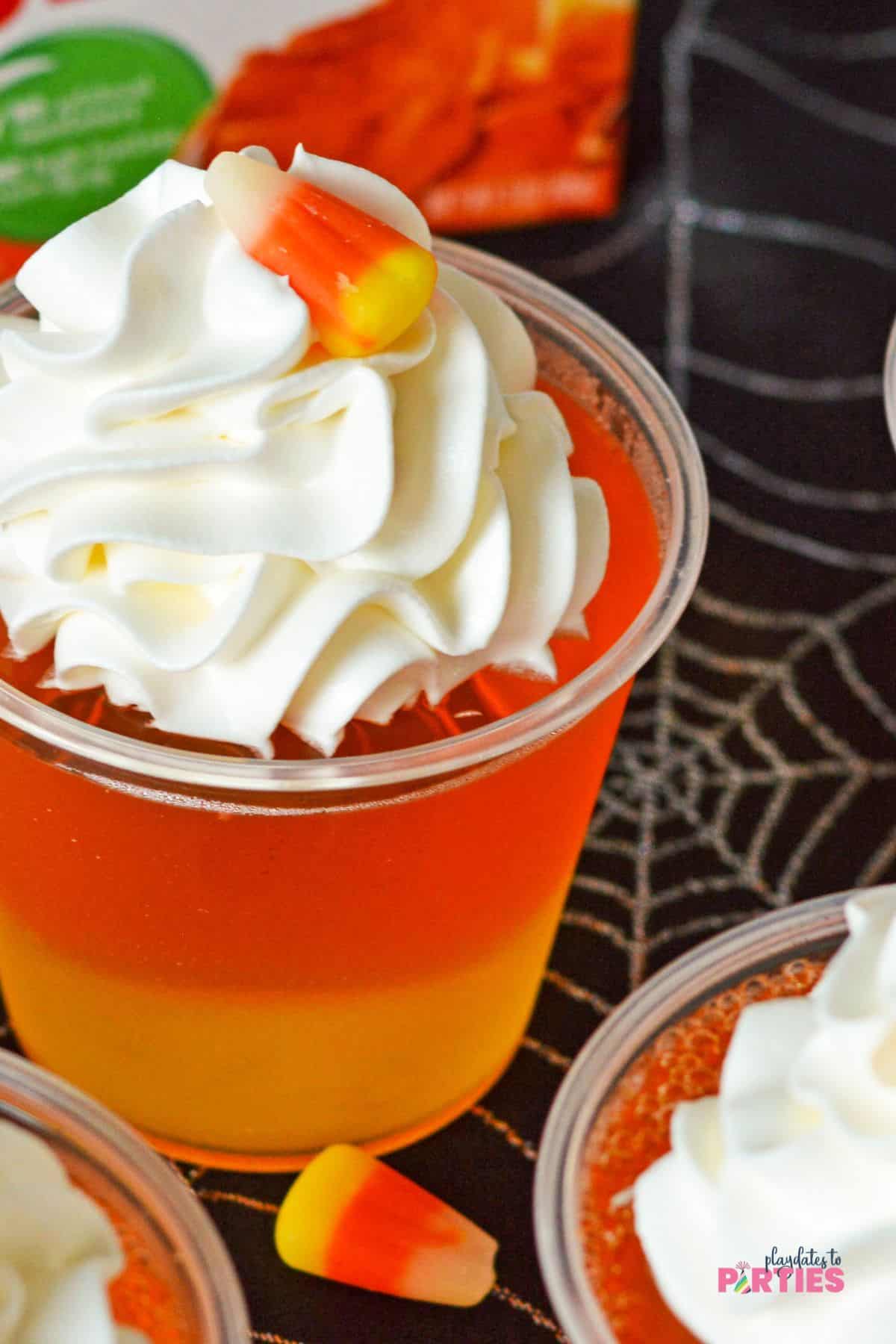 A plastic cup with layers of pineapple and orange jello with whipped cream on top.