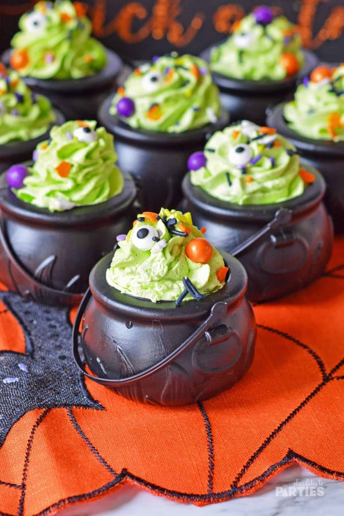Pudding snacks in black plastic pots with green whipped cream and sprinkles.