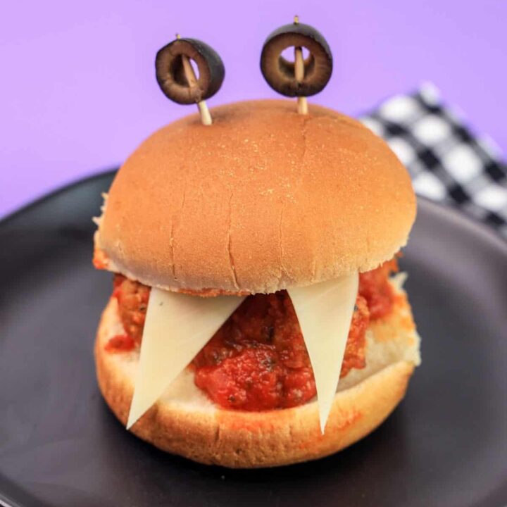 A monster sandwich with meatballs and olive eyes on a black plate.