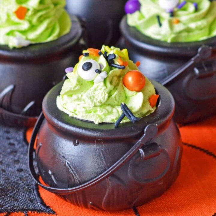 Pudding snacks in black plastic pots with green whipped cream and sprinkles.