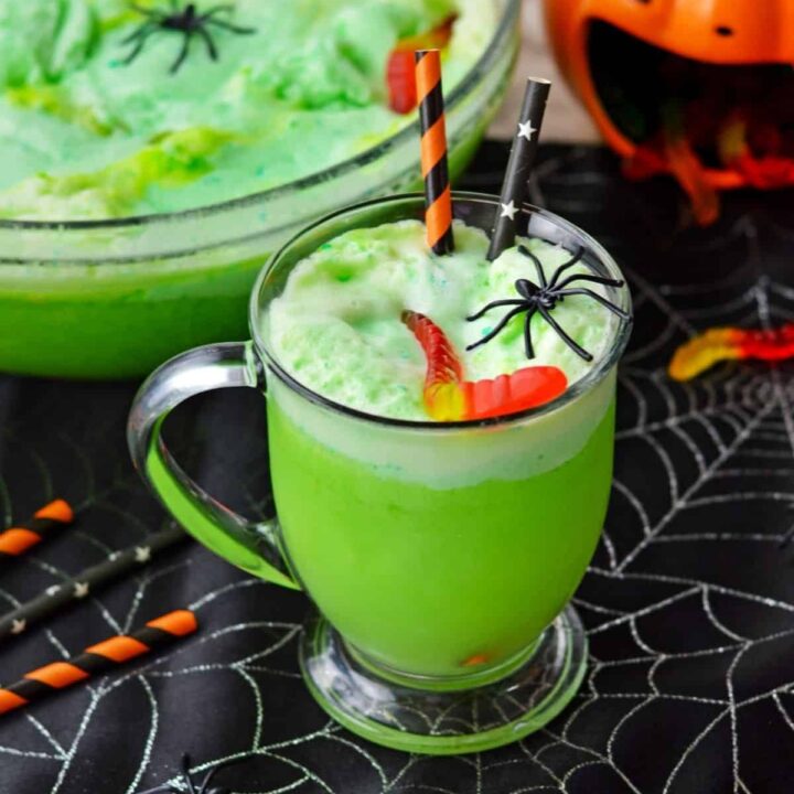 A green Halloween drink sitting near a punch bowl and Halloween party decorations.