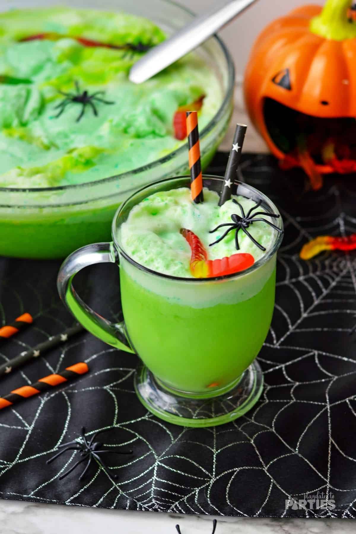 A green Halloween drink sitting near a punch bowl and Halloween party decorations.