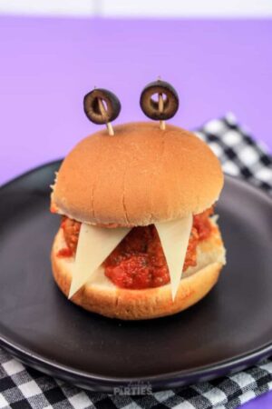 Two triangle cheese teeth stick out of a monster meatball slider with olives on top for eyes.