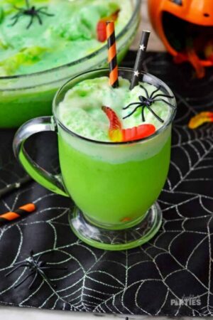 A green Halloween drink sitting near a punch bowl and Halloween party decorations.