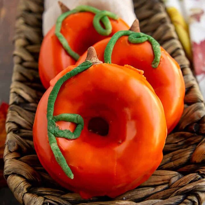 Donuts with orange glaze and decorated to look like pumpkins are arranged in a single row on a tray.