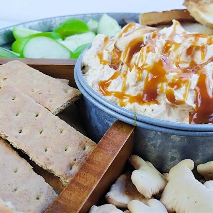 A bowl of pumpkin spice fluff dip is surrounded by cookies and apple slices for dipping.