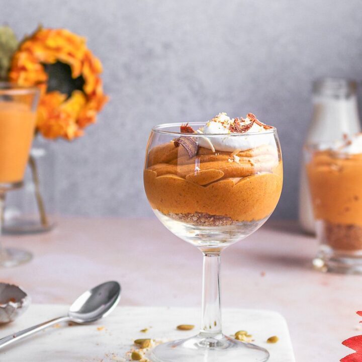 A wine glass is filled with coconut cream pumpkin mousse and sits on marble cutting board.