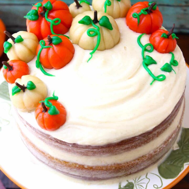 A raw edged pumpkin layer cake is decorated with white and orange candy pumpkins.