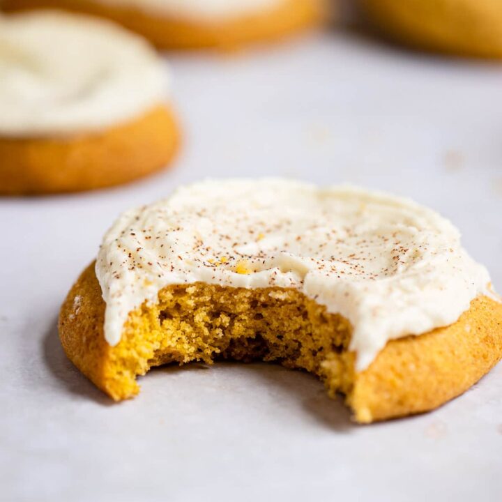 A frosted pumpkin cookie with one bite taken out.