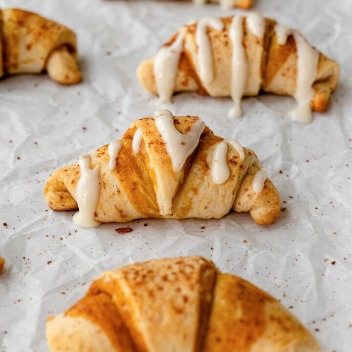 Pumpkin cream cheese crescent rolls are finished with glaze as they cool on parchment paper.