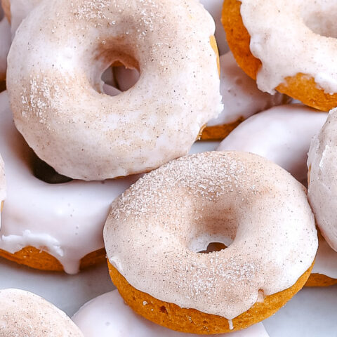 Pumpkin donuts covered with white glaze and sparkling sugar.