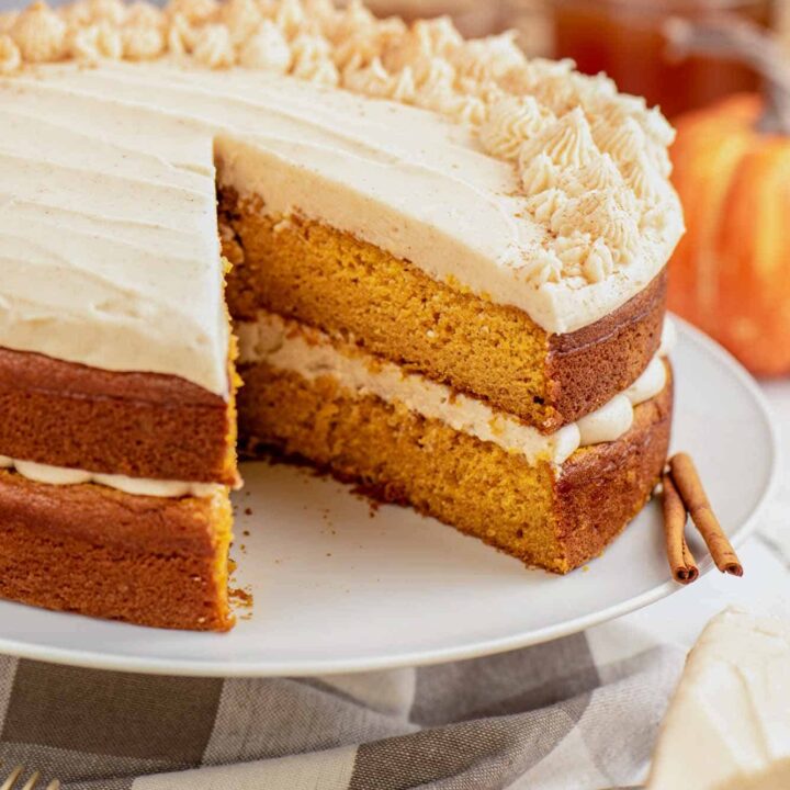 A pumpkin layer cake with one slice removed sits on a white cake stand.