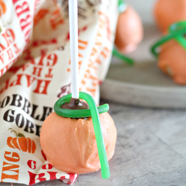 A pumpkin shaped cake pop sitting on a Thanksgiving tea towel.