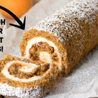 A pumpkin roll cake dusted with powdered sugar and sitting on a piece of parchment paper.