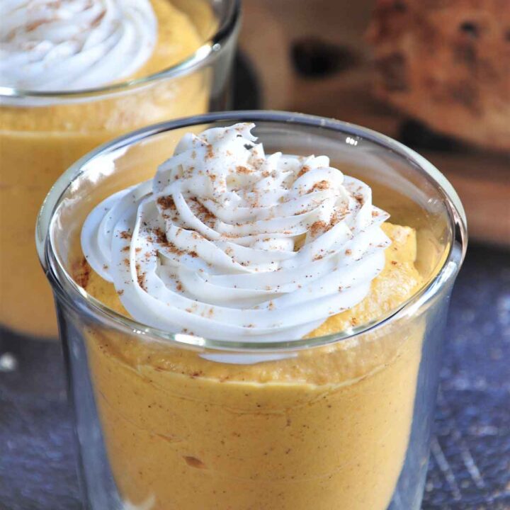 A cup of pumpkin mousse is topped with whipped cream and pumpkin spice.