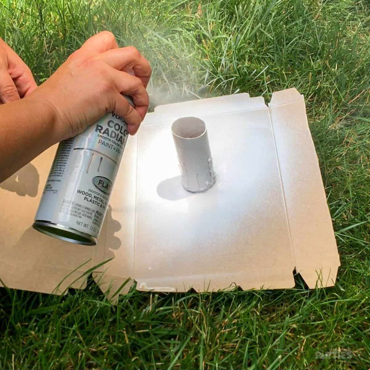 Spray painting a toilet paper tube with white paint.