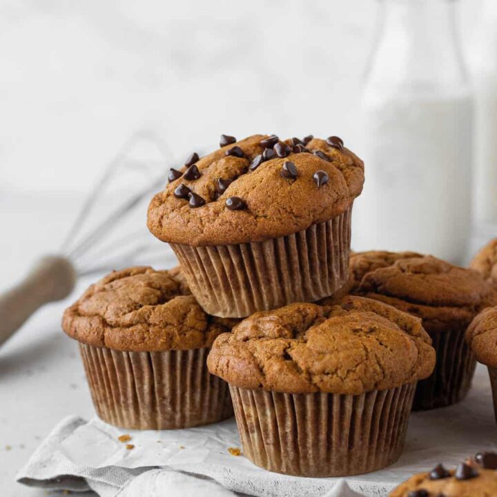 Pumpkin muffins stacked on a tea towel with a jar of milk nearby.