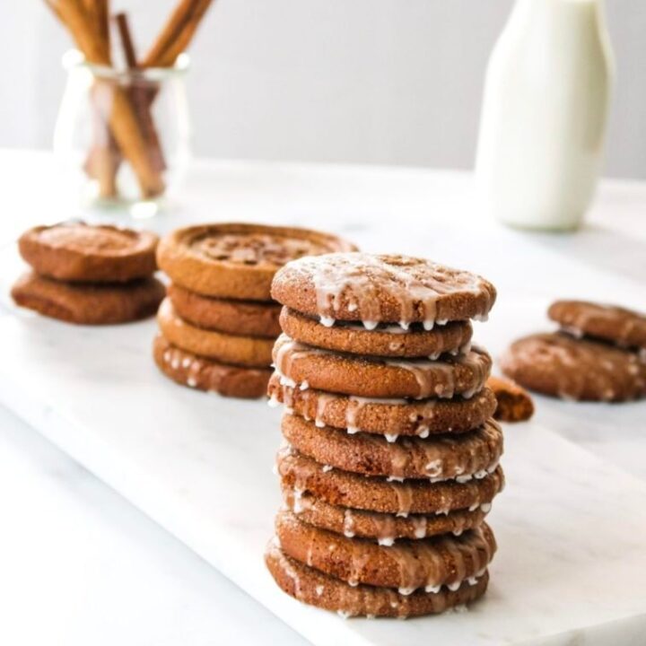 Stacks of pumpkin snap cookies are decorated with a glaze placed on a marble board.