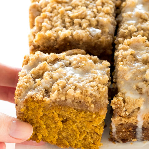 A woman's hand grabbing a square of pumpkin spice coffee cake from a tray.
