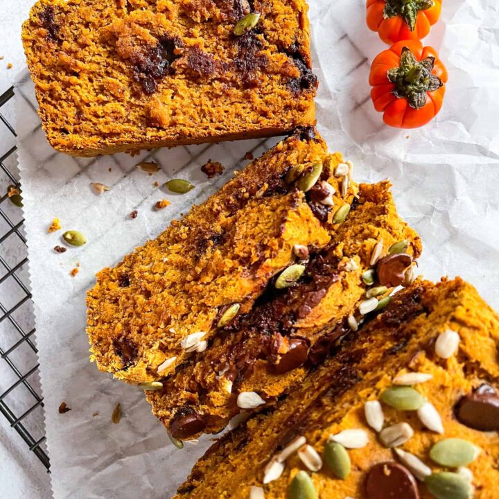 Vegan pumpkin bread sliced on parchment paper and topped with pumpkin seeds.