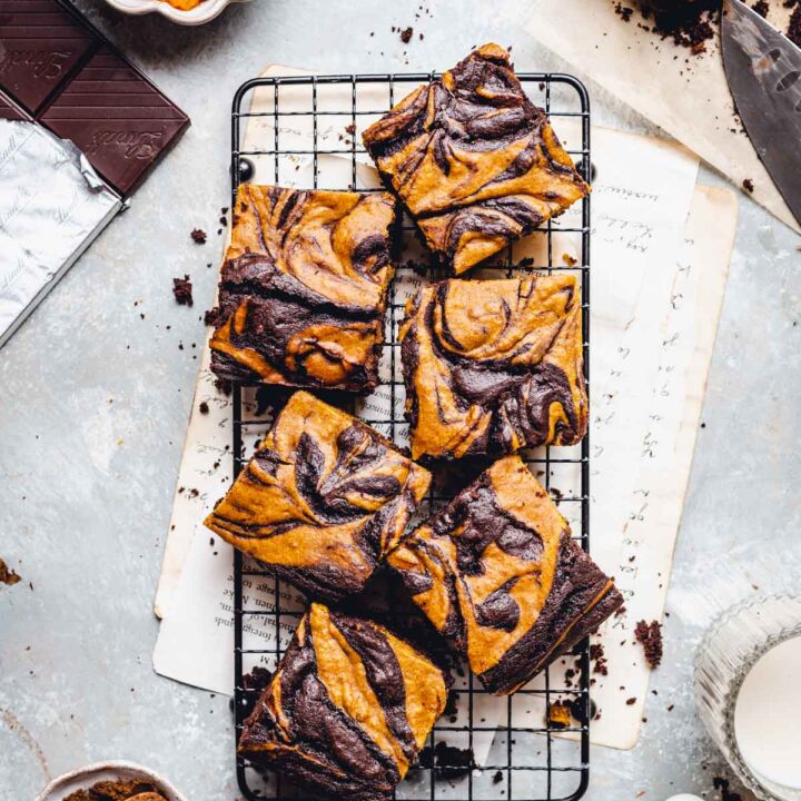 Vegan pumpkin swirl brownies are on a cooling tray and surrounded by brownie ingredients.