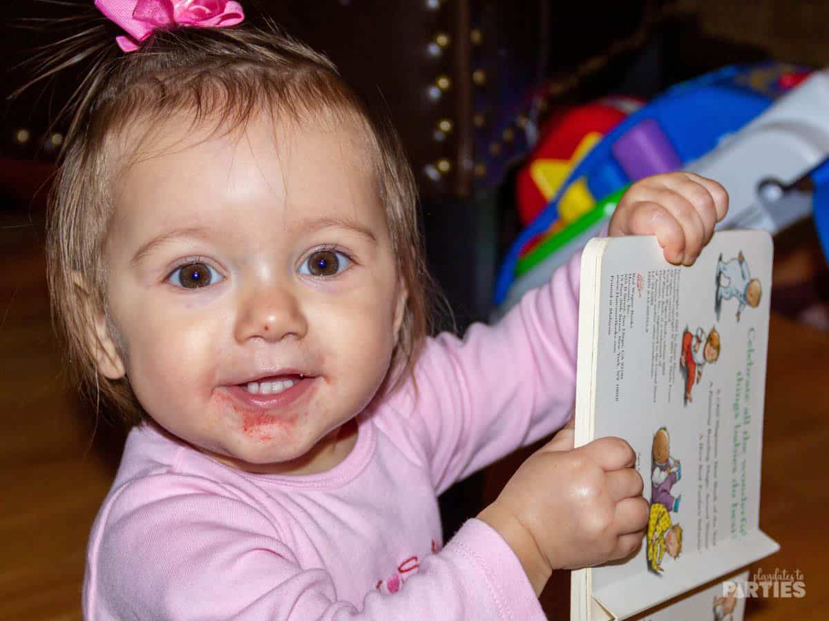 A toddler girl playing with a board book.