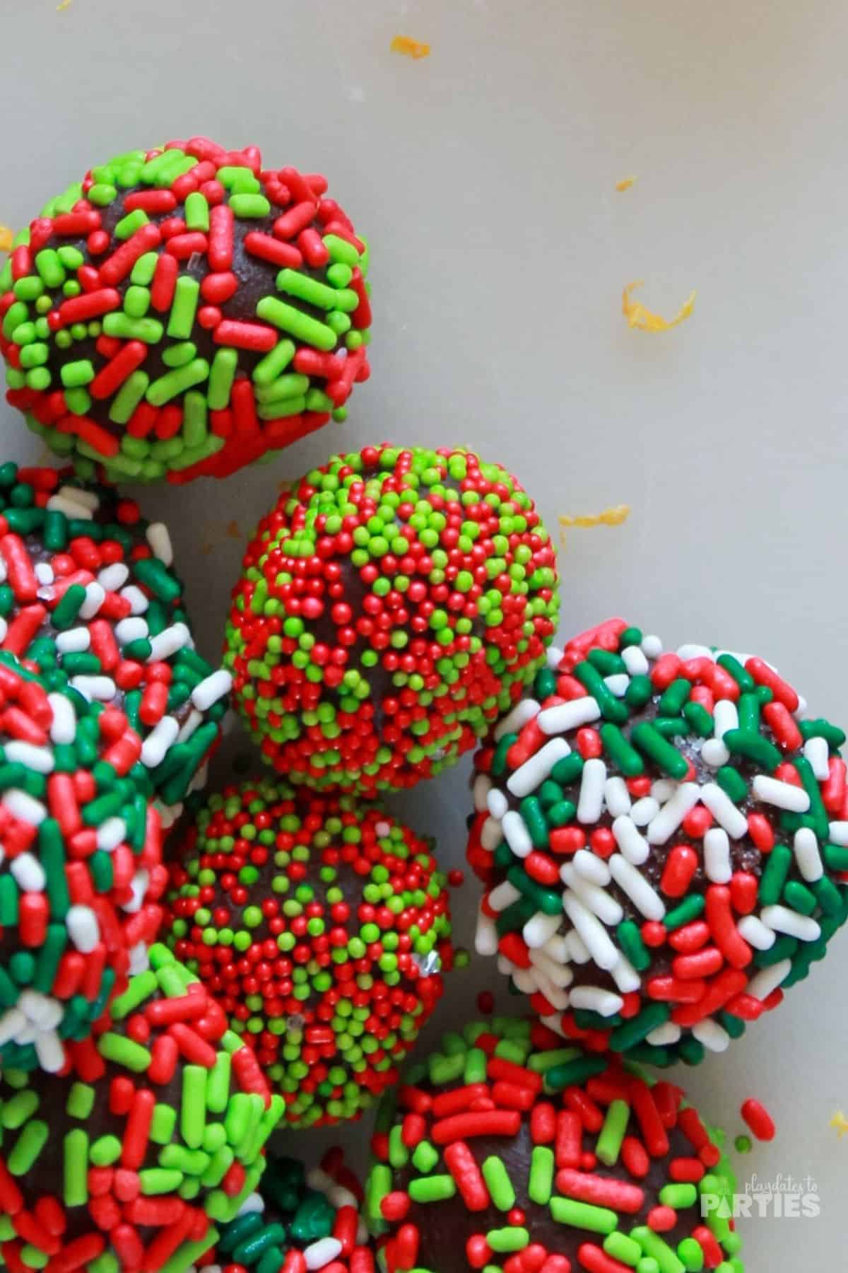 A pile of dark chocolate truffles made with liquor and coated in red and green sprinkles.