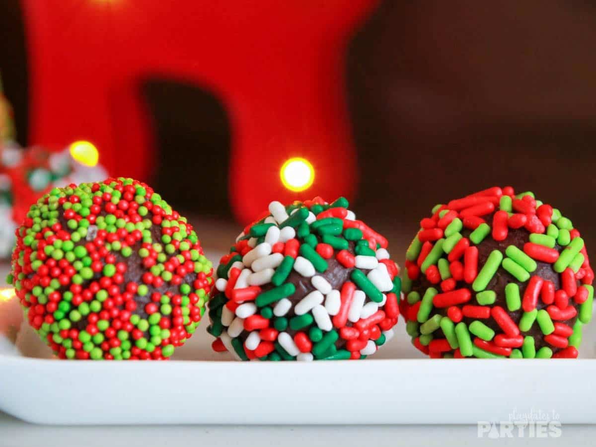 Three handmade chocolate truffles sit on a small tray with Christmas decorations in the background.