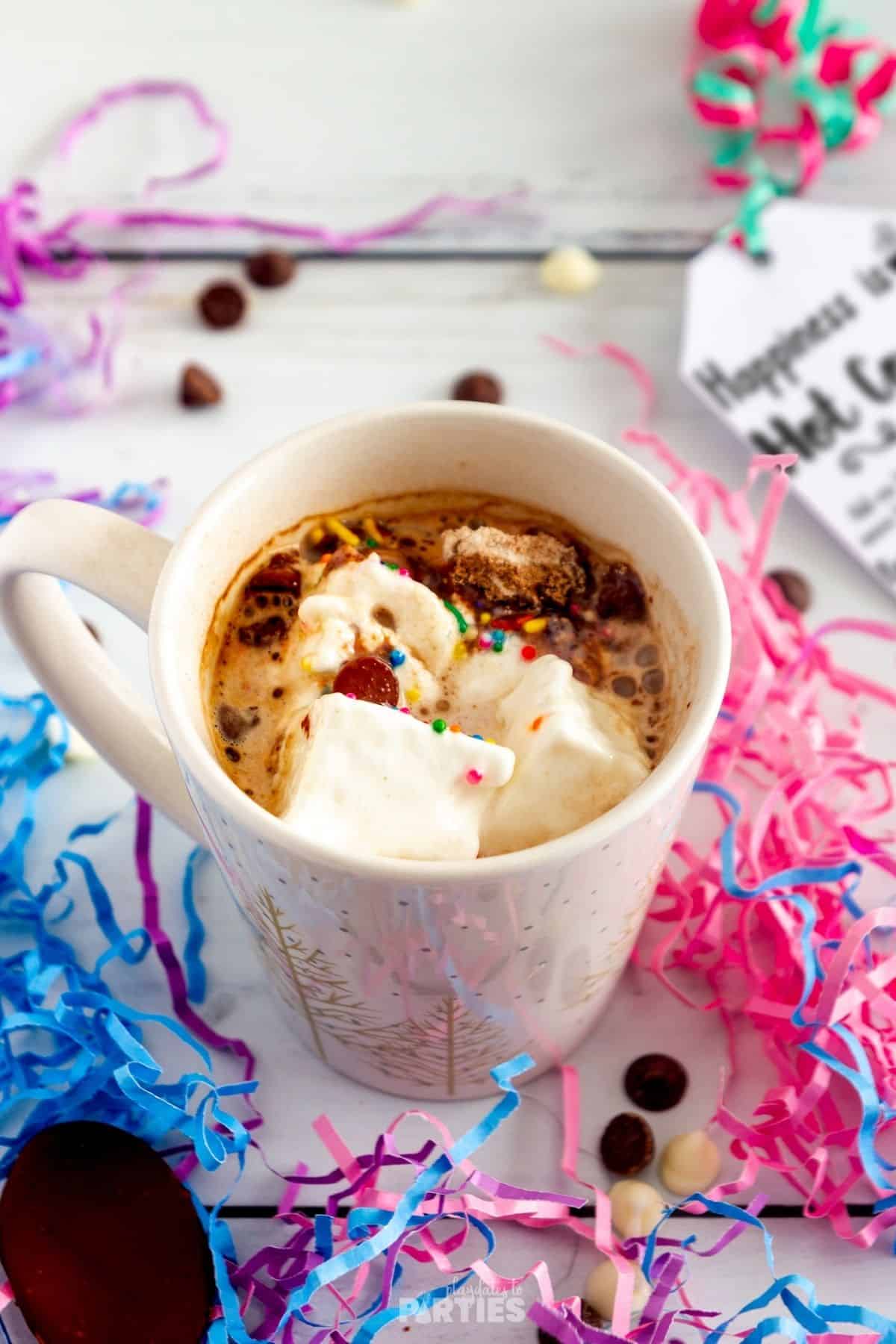 A mug of hot chocolate is surrounded by party decorations.