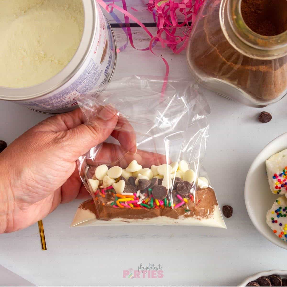 A cellophane bag shows layers of powdered milk, hot cocoa, sprinkles, and chocolate chips.